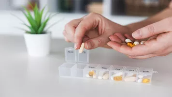 closeup of Caucasian woman's hands adding pills to pillbox