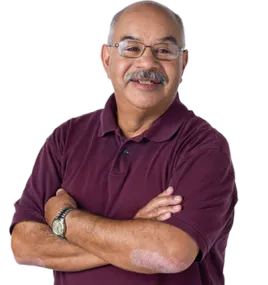 Older hispanic man with glasses and a gray mustache. His arms are crossed in a relaxed manner and he's wearing a short sleeve maroon polo shirt and a watch. 