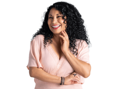 Woman with dark curly hair smiles and touches her face