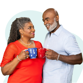 African American couple gazing lovingly at each other and clinking mugs. Woman is wearing a red shirt and holding a blue mug, man is wearing a light blue shirt and holding a red mug.