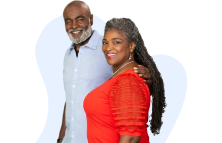 African American couple facing camera and smiling while walking together. He's wearing a light blue button down shirt and has his arm around her, and she's wearing a red blouse.