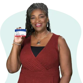 African American woman in dark red dress holding her Medicare card and smiling.